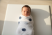Newborn baby swaddled in a white blanket with blue patterns on a light surface