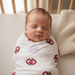 Peaceful newborn baby swaddled in University of Oklahoma Sooners muslin swaddle blanket in crimson and cream, cozy nursery lifestyle shot showing premium OU baby swaddle in use

